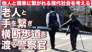 杖を持つ老人と手を繋いで横断歩道を渡る警察官