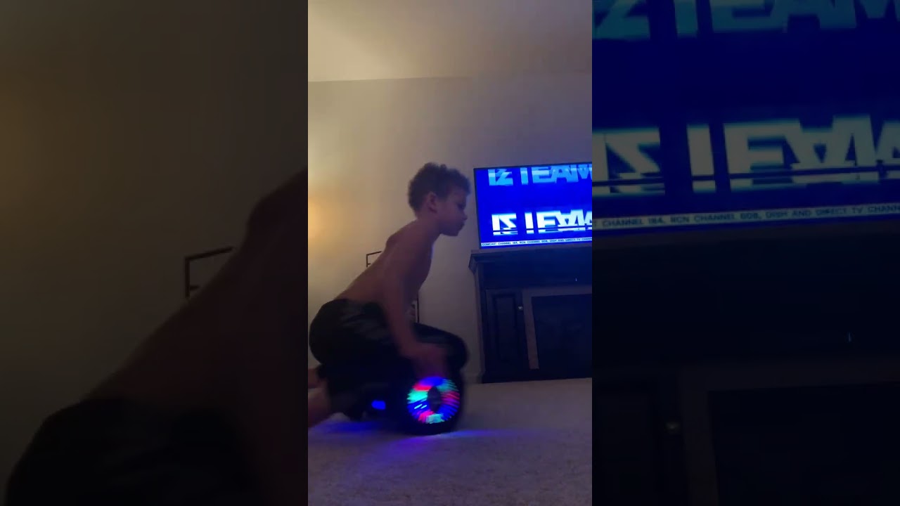 Little boy does long spin on hoverboard sitting on knees in living room in front of TV