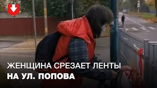 Люди спорят с женщиной, которая срезает ножом бело-красно-белые ленты на ул. Попова в Минске