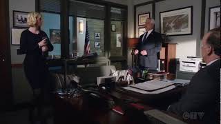 Abigail Hawk walking into an office room in a black mini dress, white pearls and nylons