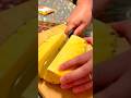 cutting a fresh peeled pineapple into two large vertical slices on a wooden board