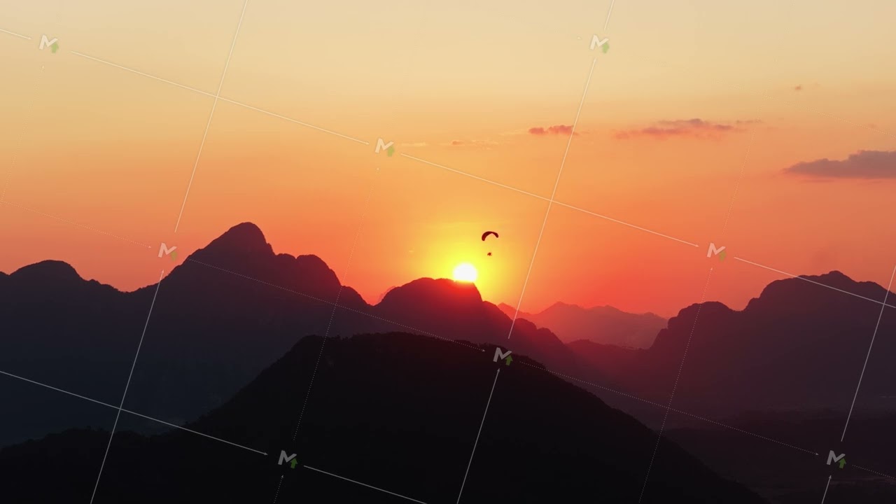 Tripod aerial shot of hot air balloon floating above a mountain range in Laos during a golden sunset