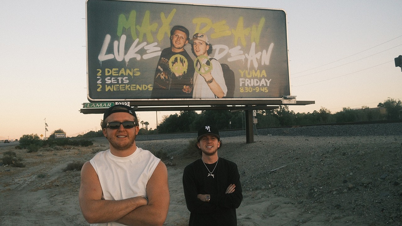 Max Dean and Luke Dean photographed in front of their Coachella billboard — still from BEHIND THE DEANS, published on the artist's own YouTube channel
