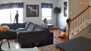Girl holding blanket walks downstairs while boy in yellow shirt falls behind her (Security camera)