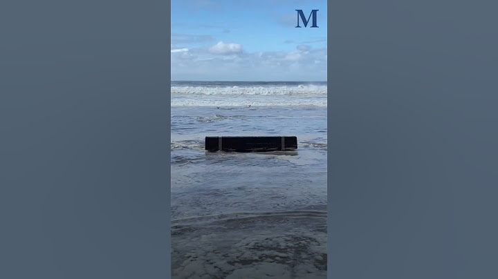 Waves surge across sand, swarm cars in parking lot at Austinmer Beach