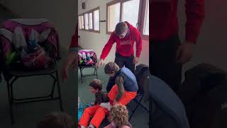 Boy buckles ski boots while standing on chair then falls and accidentally kicks brother on face
