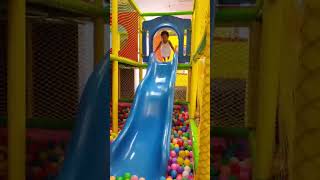 Girl jumps from top of blue slide into ball pit
