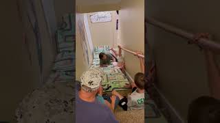 Family places long mat on stairs then little girl falls backwards and flips down steps
