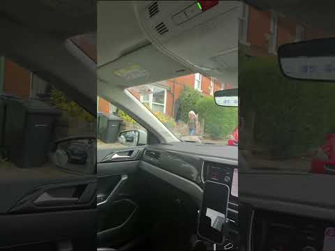 A driver's view of a narrow road with parked cars on one side and an oncoming vehicle approaching the gap.