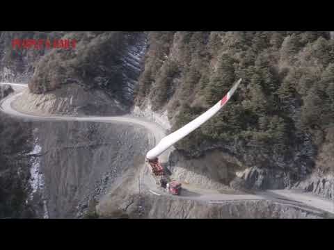 A truck carrying a massive wind turbine blade navigates a treacherous mountain road