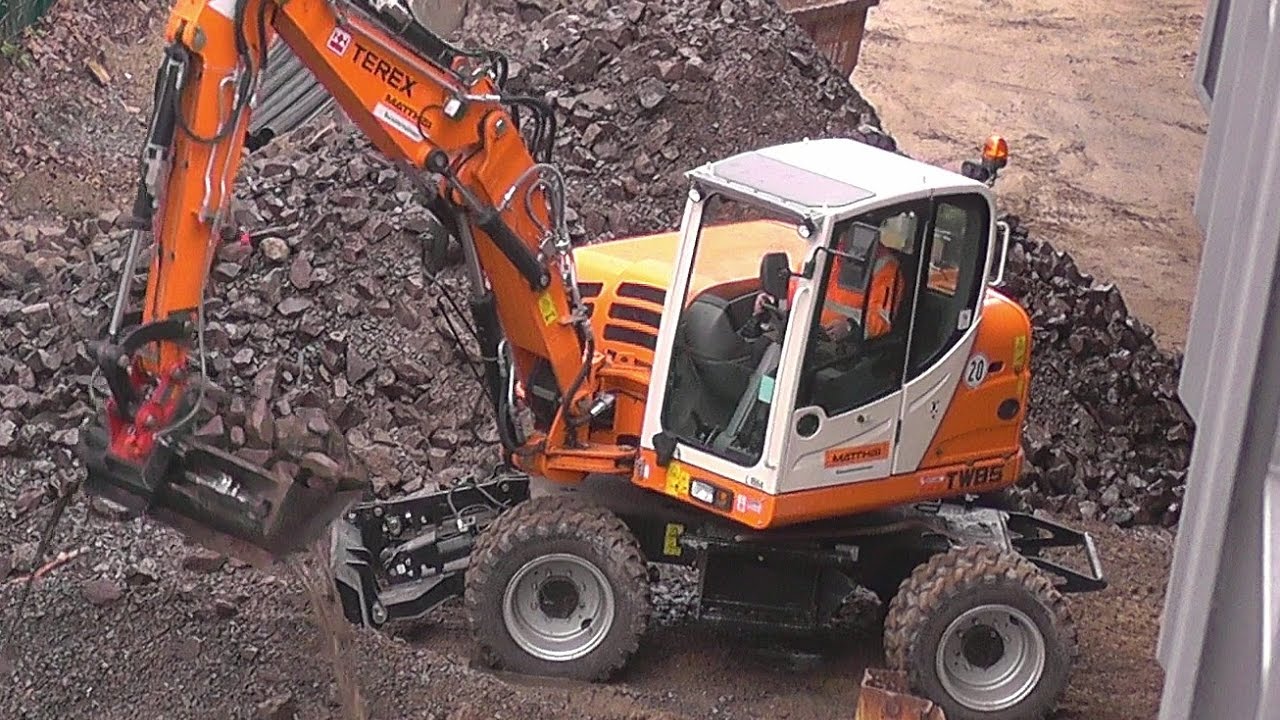 Terex Bagger TW85 entfernt Steine und Sand am Flussufer.