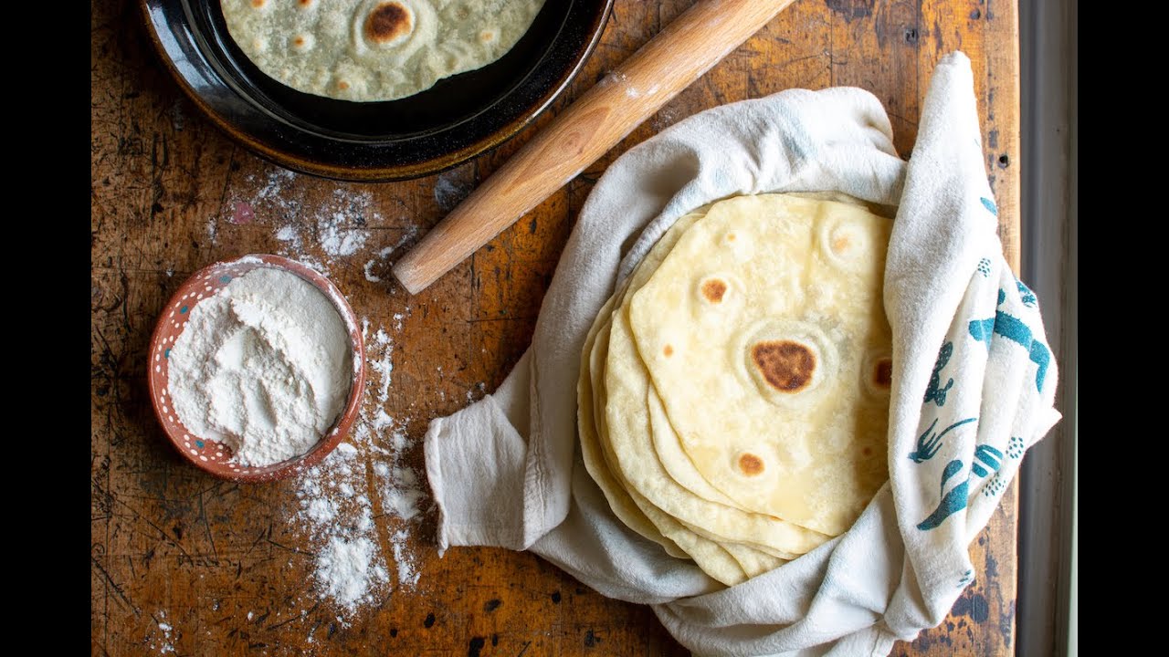 Woman makes corn tortillas by hand and cooks them on a large clay