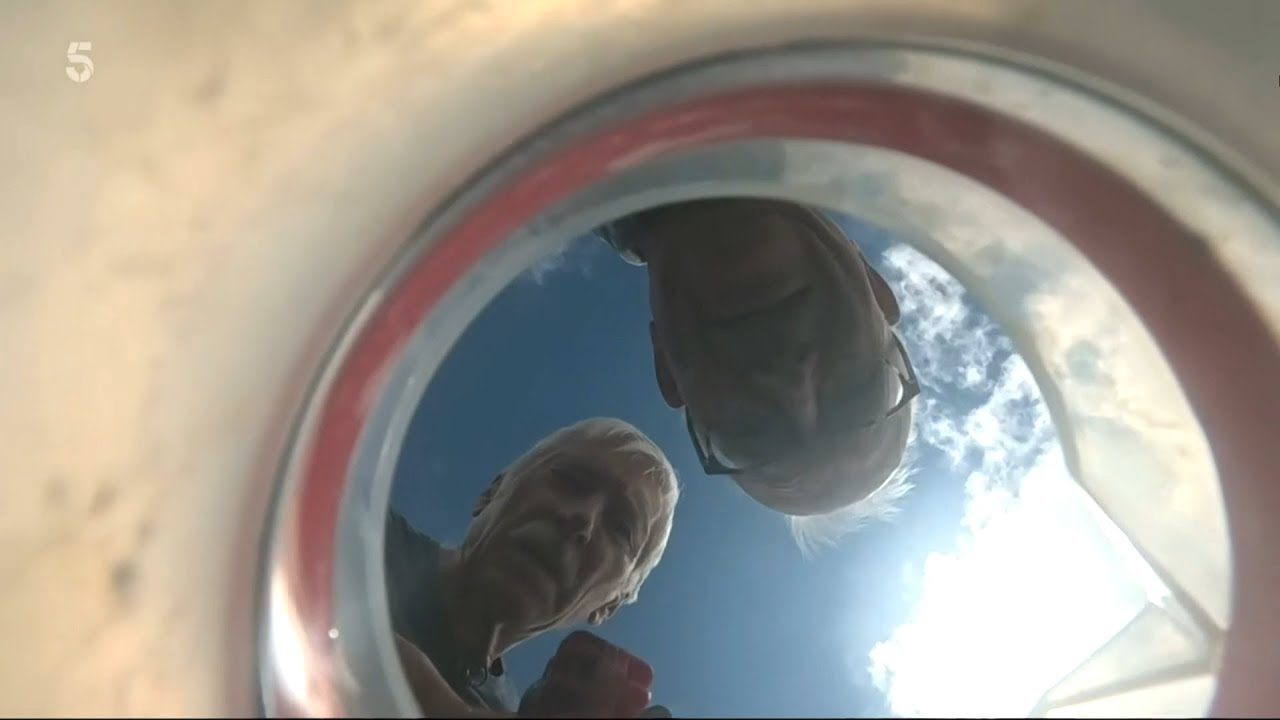Two men peering into a beaker of water. The shot is taken looking up from the bottom of the beaker.