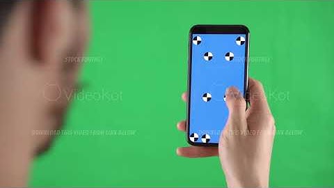 Man is zooming the content on the smartphone with tracking markers on display against a green screen
