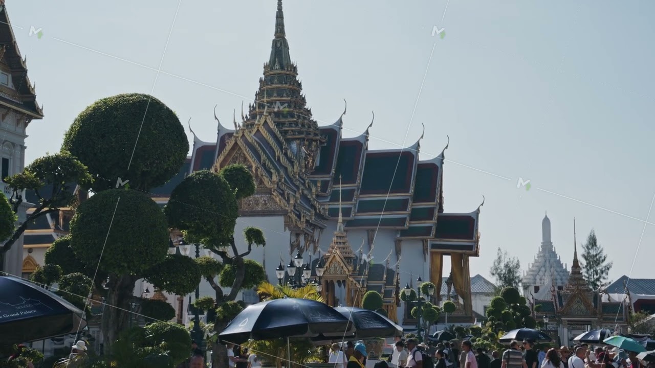 Tourists with umbrellas walk around historic Grand Palace in Bangkok. Sunny day at a famous