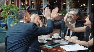 Business men and women talking in restaurant then doing high-five during successful talks