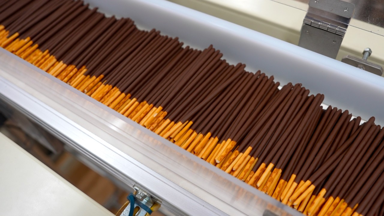 ポッキーを大量生産するプロセス。1966年発売！世界に展開する棒状チョコレート菓子を作る日本の工場。
