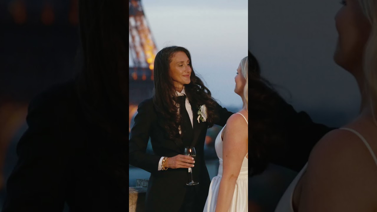 Two brides toast on a Paris balcony at dusk, with the Eiffel Tower glowing behind them