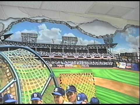 This video portrays a hand-painted wall mural by the artist Bonnie Siracusa. This mural was painted by the artist in the Ryder Retail Station Post Office in Brooklyn, New York. Featuring the Brooklyn Dodgers, this wall mural is of historic significance as it documents baseball players, the famous Ebbets Fields, and the important attention to detail of the famous right field advertisements and baseball memorabilia from a time fondly remembered by New Yorkers. The wall mural uses a technique called trompe l'oeil (pronounced tromploy) to create the illusion that the wall has been cracked open and you can step into the mural and join the players on the baseball diamond at Ebbets Field. The artist, Bonnie Siracusa, painted herself in the corner of the mural, portrayed painting the mural. Ebbets Field was a Major League Baseball Park located in Flatbush, New York (now Crown Heights) and the home of the Brooklyn Dodgers. In 1960, Ebbets Field was destroyed and replaced by apartment buildings but fond memories of the baseball played their lives on.