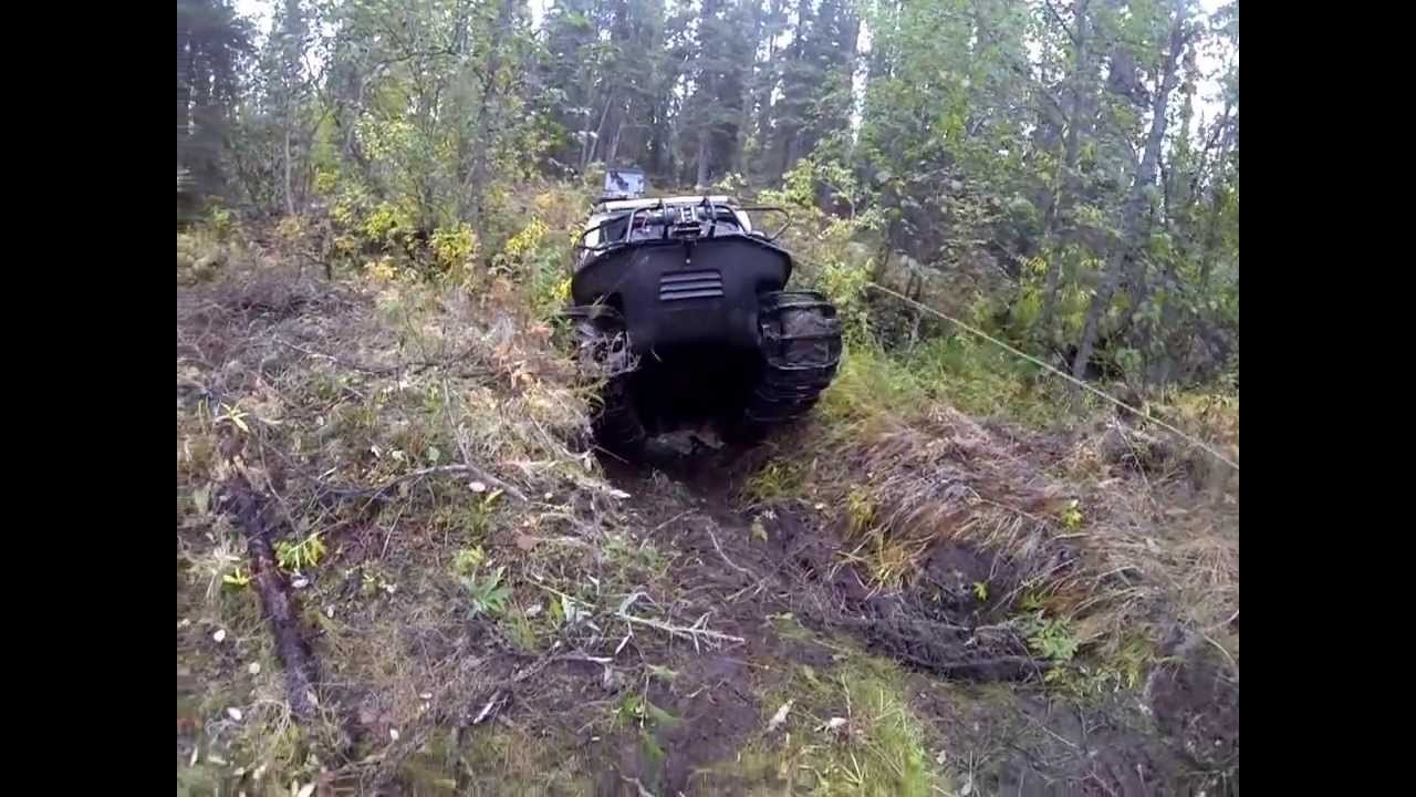 Argo with tracks climbs steep bank from creek while towing trailer