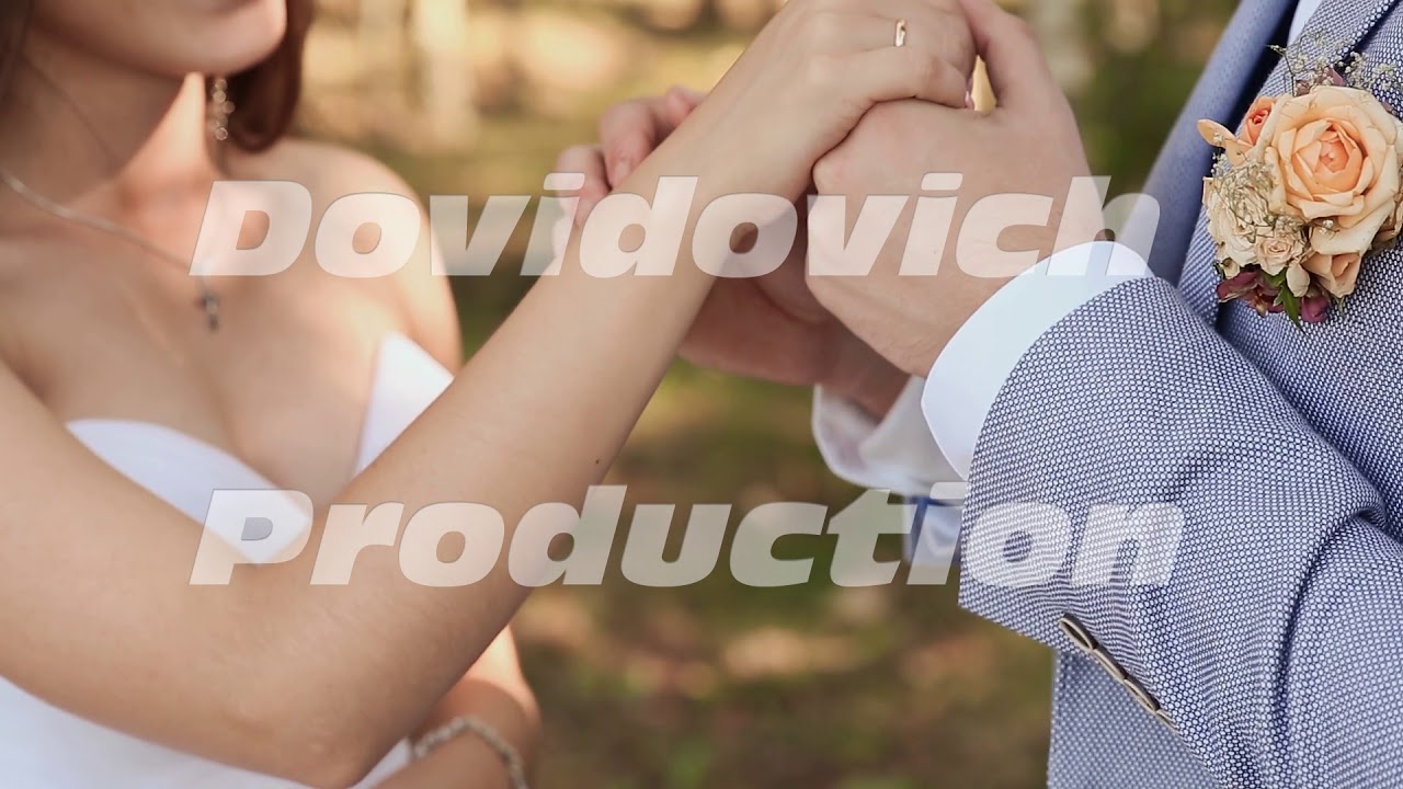 The bride and groom exchange wedding rings against a background of green nature. The groom puts the