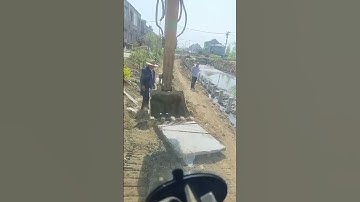 An excavator installs a concrete slab for a fence enclosing a river