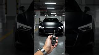 Matte black Audi R8, black carbon smart key, hand holding key near lens, car standing front view, ci