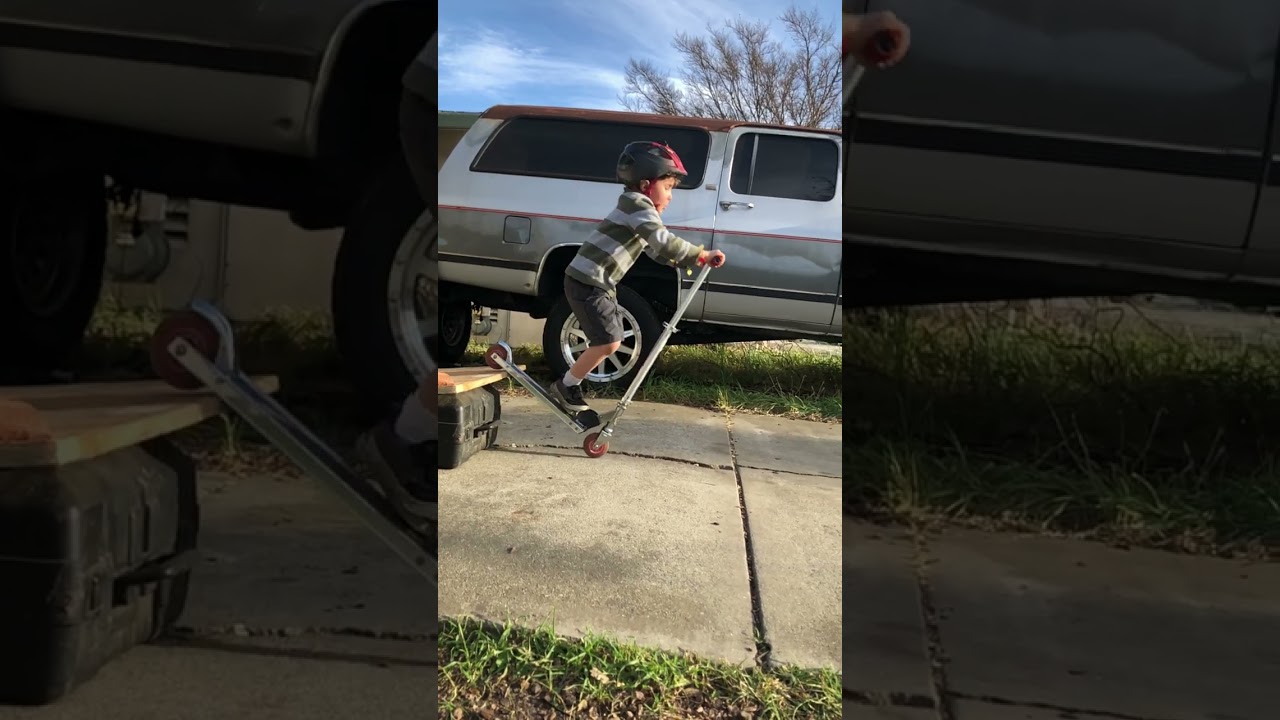 Boy jumps homemade wooden ramp on scooter but doesn't pulls up then falls forward and faceplants