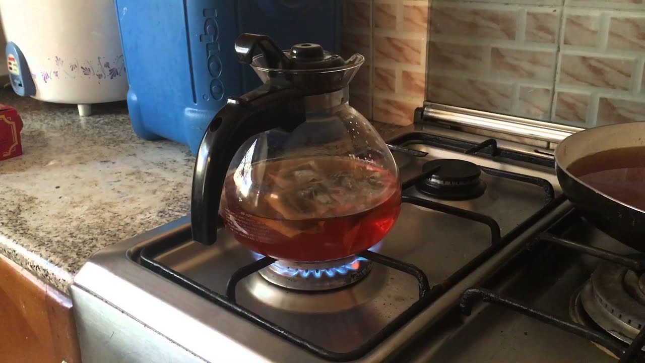 Red tea drink is boiled in a glass kettle on a gas stove, close-up