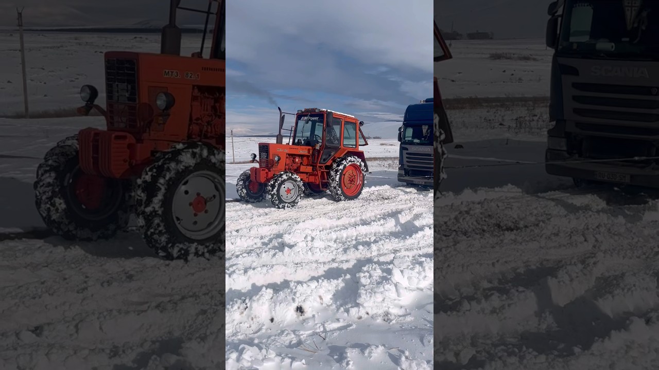 Трактор тянет грузовик по заснеженной местности.