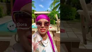 Selfie-camera POV. Baba Zina holding the phone, smiling with an unnatural fake Hollywood smile, sho