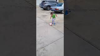 Boy in green shirt dances around soccer ball then tries tokick it but falls on top of it