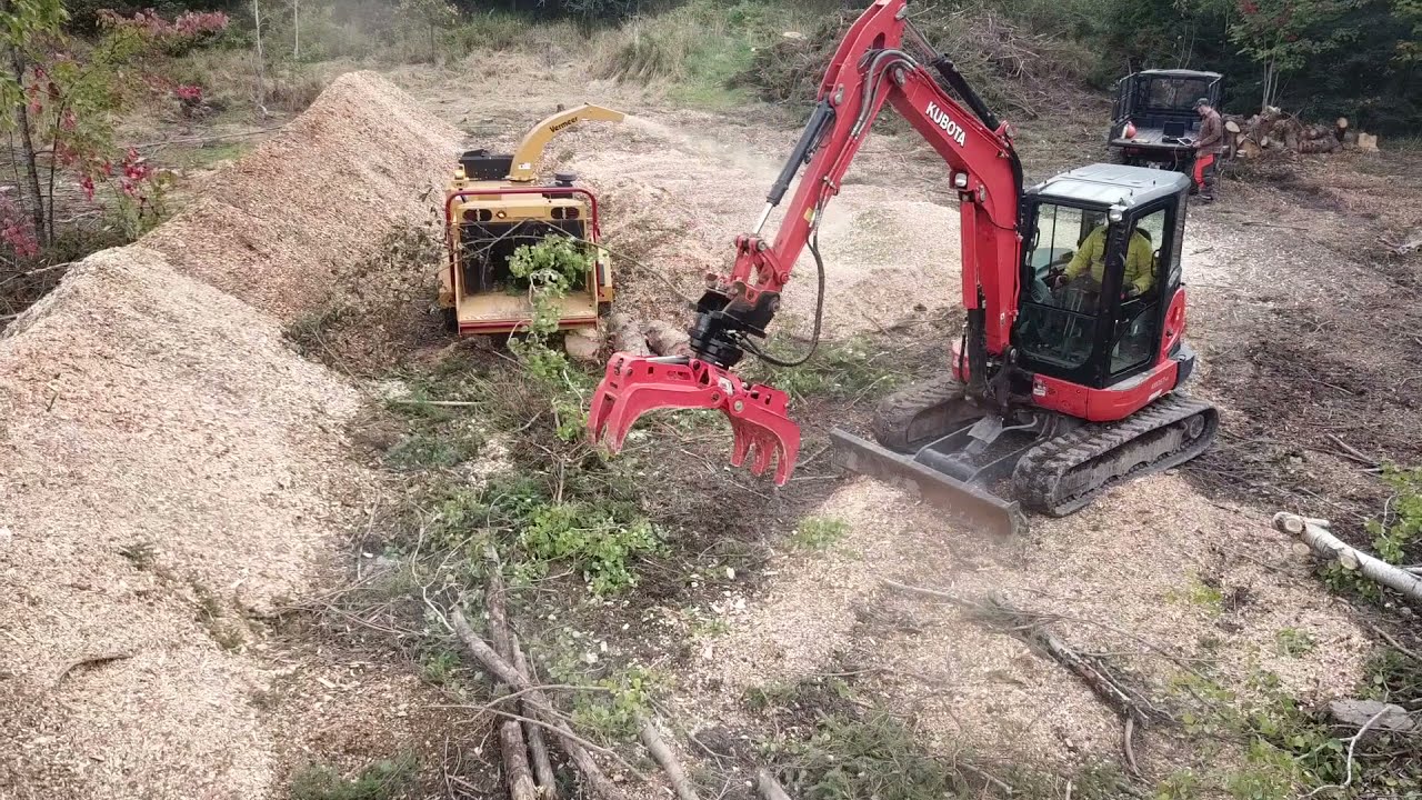 Excavator with Rotobec rotating grapple feeding trees into Vermeer BC1200XL Chipper