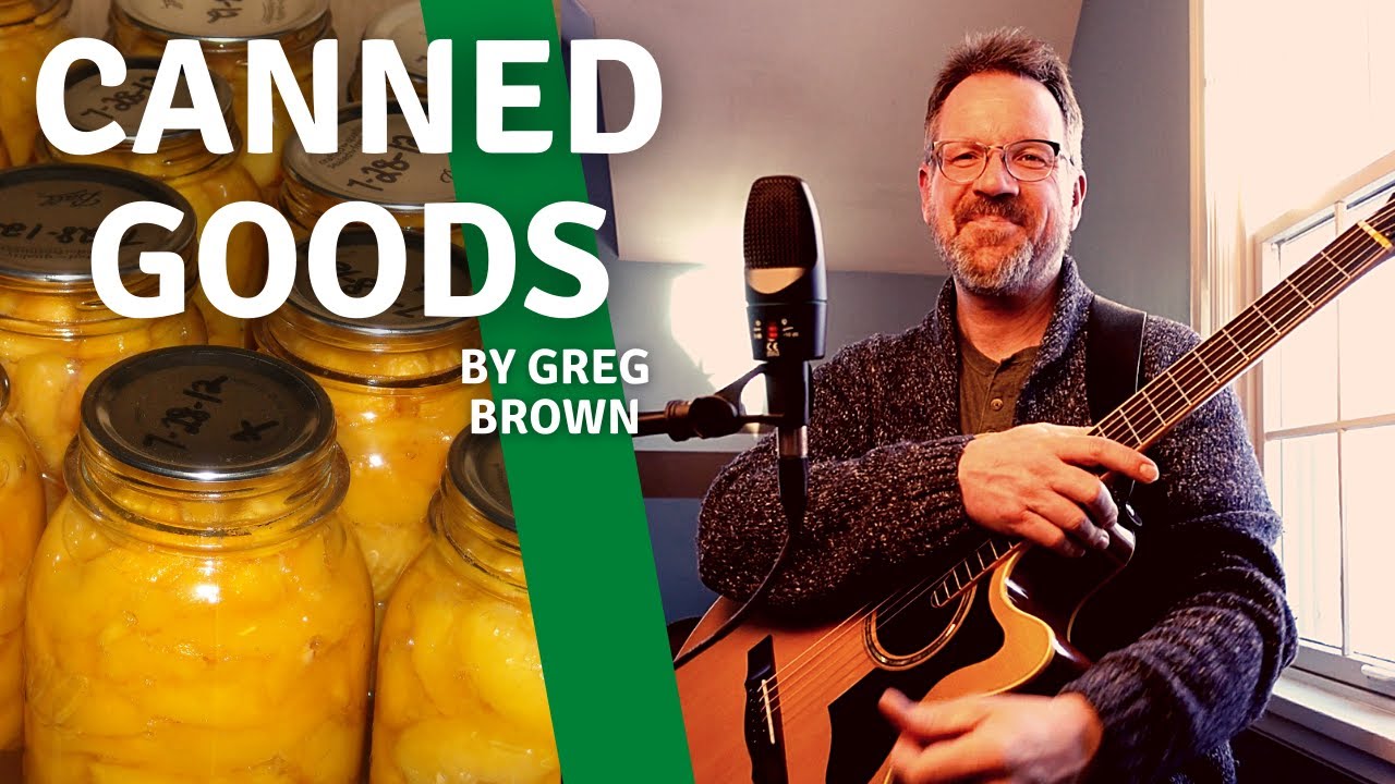 Canned Goods by Greg Brown. With Guitar, Mandolin and a brush on a book