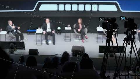 Panel discussion on stage with cameras and audience at conferenc