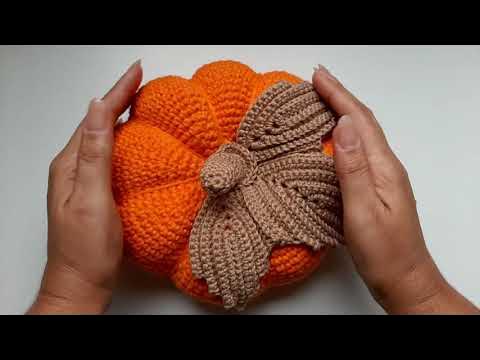 Uma boneca de crochê com roupa laranja e segurando abóboras