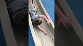 Boy goes down slide while on piece of cardboard then sneakers cause him to fall and hits edgex