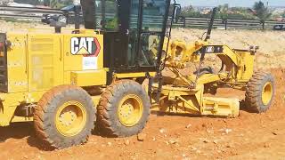 Caterpillar 140k Grader is spreading and leveling reddish brown material with big stones