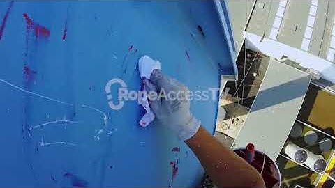 Rope access technician painting a commercial building with paintbrush and paint roller