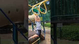 Boy attempts to climb monkey bars at the playground while Dad gives a motivational speech but falls