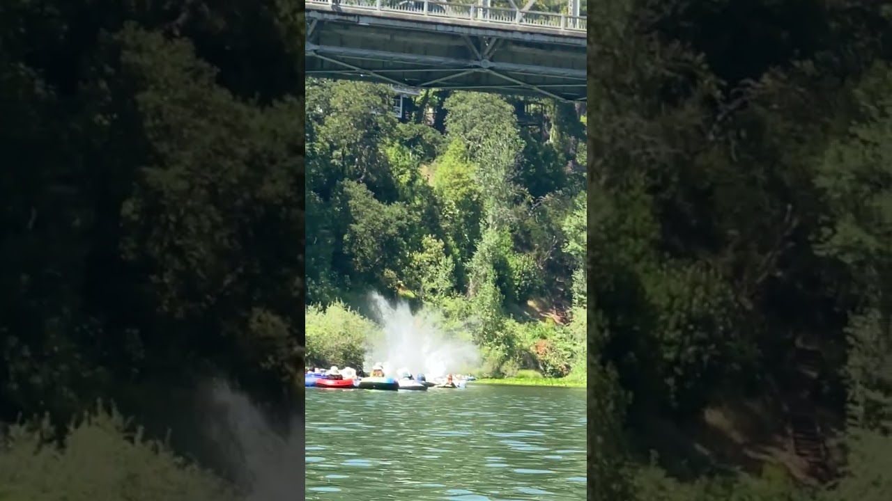 Guy jumps off bridge into ocean while his friend are on a boat in the water