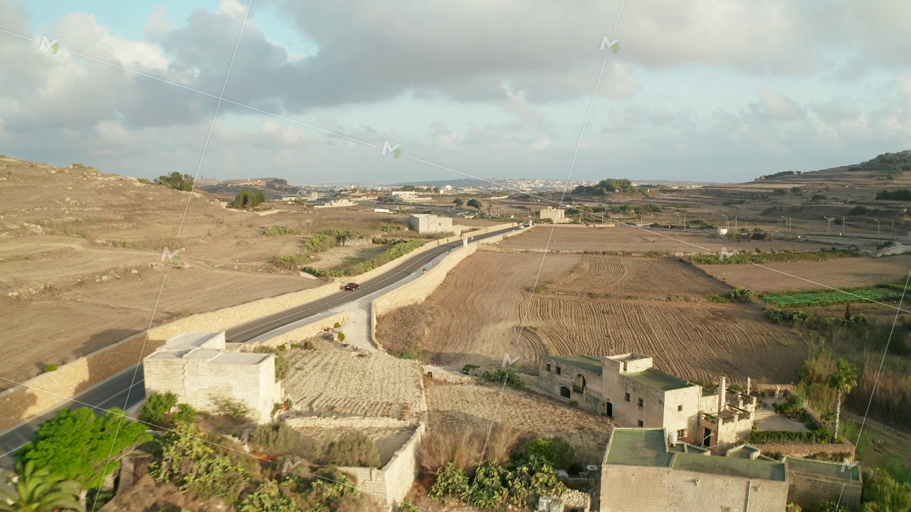 Single Red Car driving on Empty road through Rural Mediterranean Landscape on Gozo Island, Malta