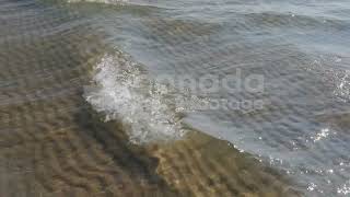 Slow motion sunlit waves in shallow water with rippled sand below stock video. HD stock video.