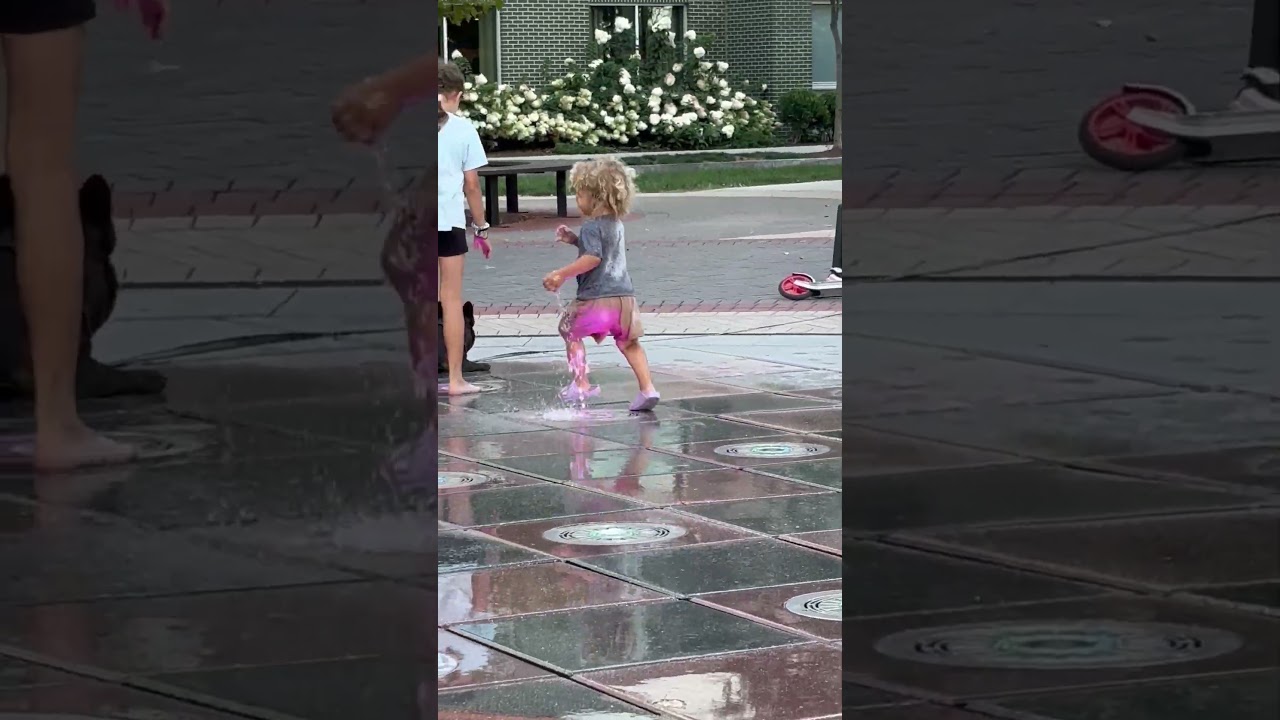Boy runs around water sprinkler park then crashes into another kid