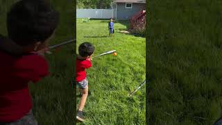 Boy uses baseball bat to hit orange ball in yard then ball hits little brother on neck near face