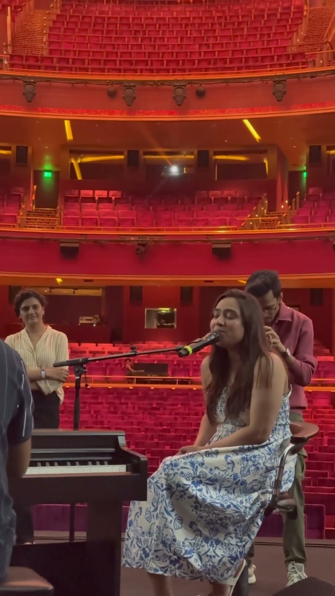 Ishani Dave singing at a microphone on a theatre stage