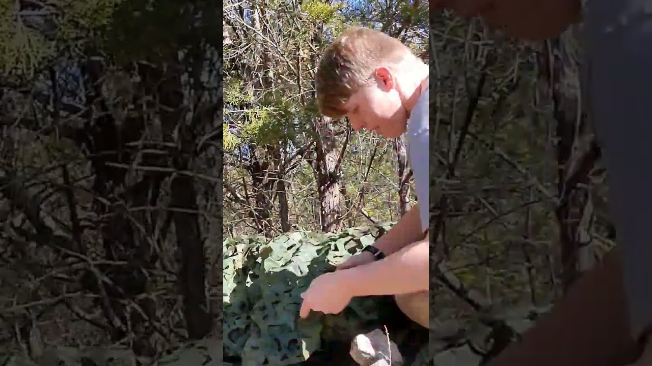 Stealth bushcraft camp under poncho and camo net 