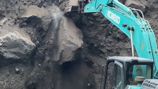 Mining sand around large rocks using Kobelco excavator heavy equipment