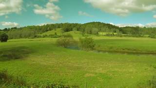 Time lapse of a country field with rolling hills, a creek and clouds moving by