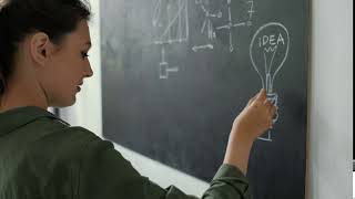 Teacher writing math formulas on blackboard and talking to her class